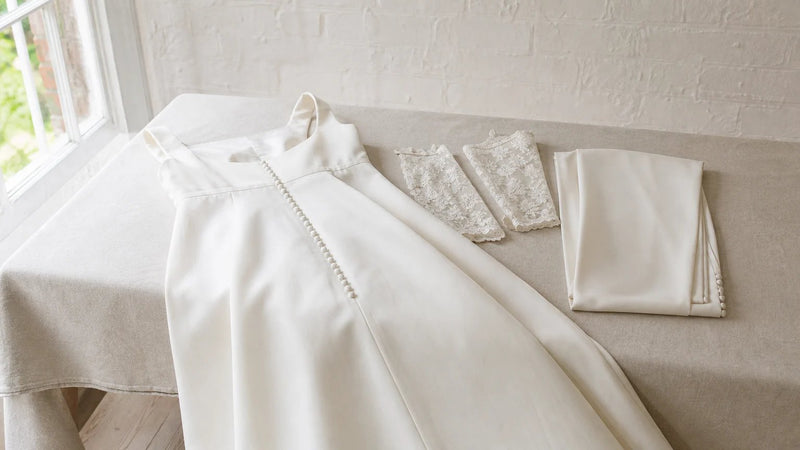 Ivory satin wedding dress with covered buttons down the back, laid out with detachable lace sleeves and a buttoned train